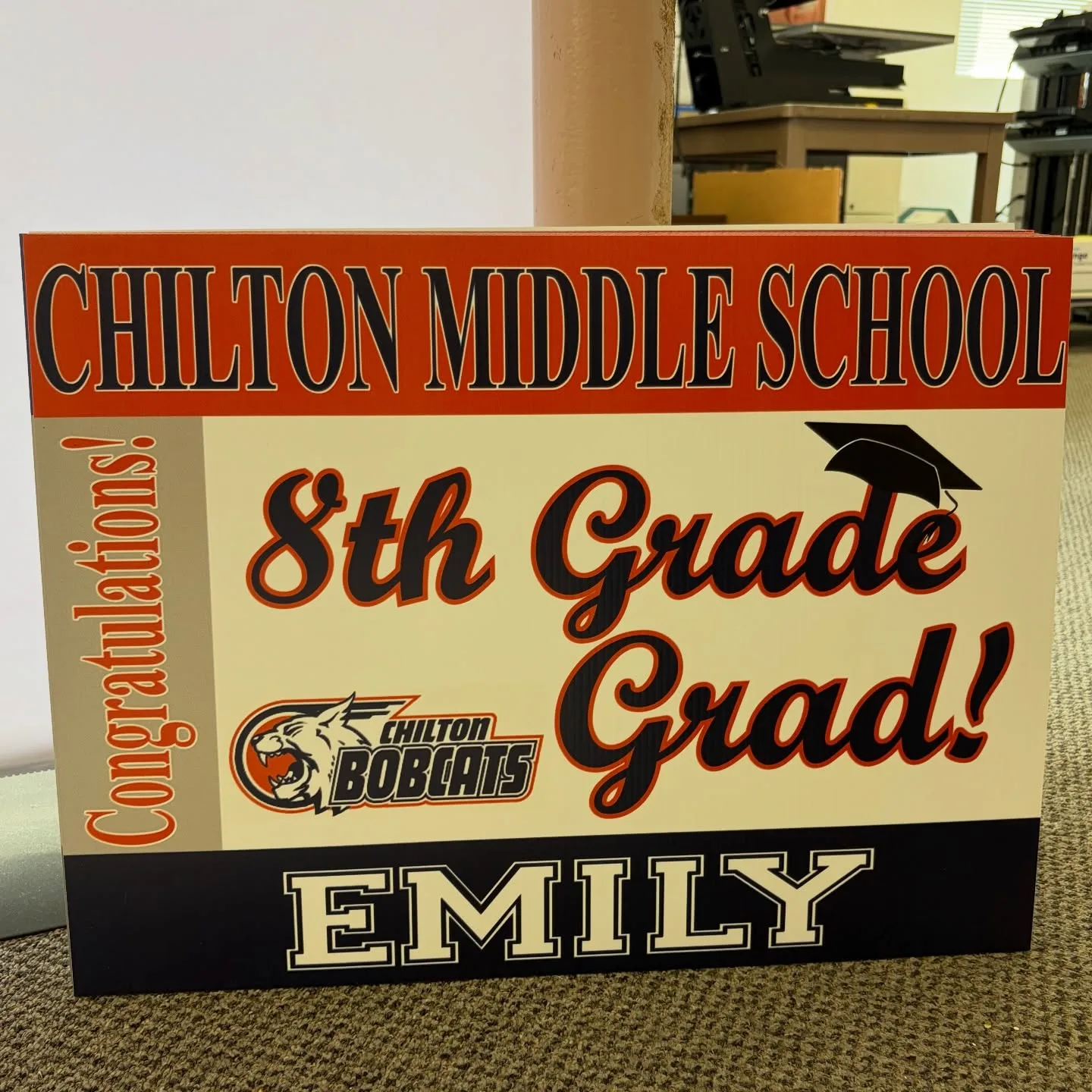 An orange-and-navy personalized graduation yard sign reading 'Chilton Middle School, Congratulations! 8th Grade Grad! Emily' with the