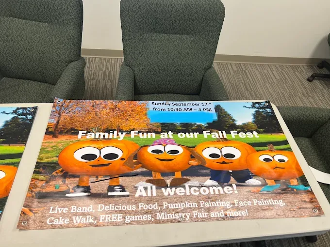 Printed vinyl banner with grommets laid across chairs in an office, advertising a church Fall Fest with cartoon pumpkin characters and