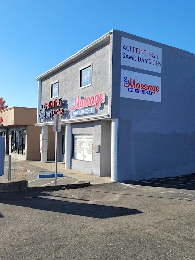 Exterior of a gray two-story corner building housing Ace Printing & Same Day Signs and SJ Massage, with rooftop channel-letter signage and